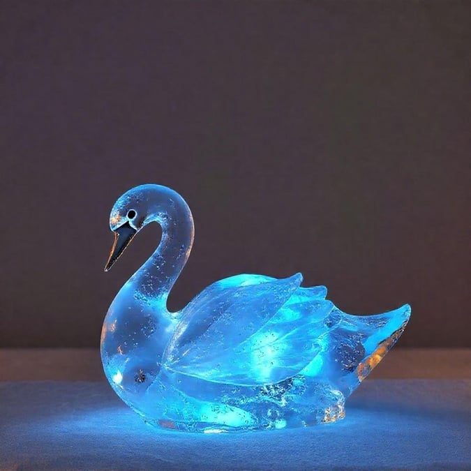 This stunning swan figurine, crafted from blue glass or crystal, exudes a mesmerizing glow that casts an ethereal light on the surrounding area. The intricate details of its form and the lifelike colors of its plumage make this piece a captivating centerpiece for any room.