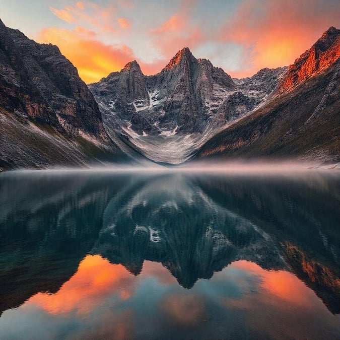 A serene view of towering mountains reflecting in the tranquil water, bathed in soft evening light. Perfect for a desktop wallpaper.