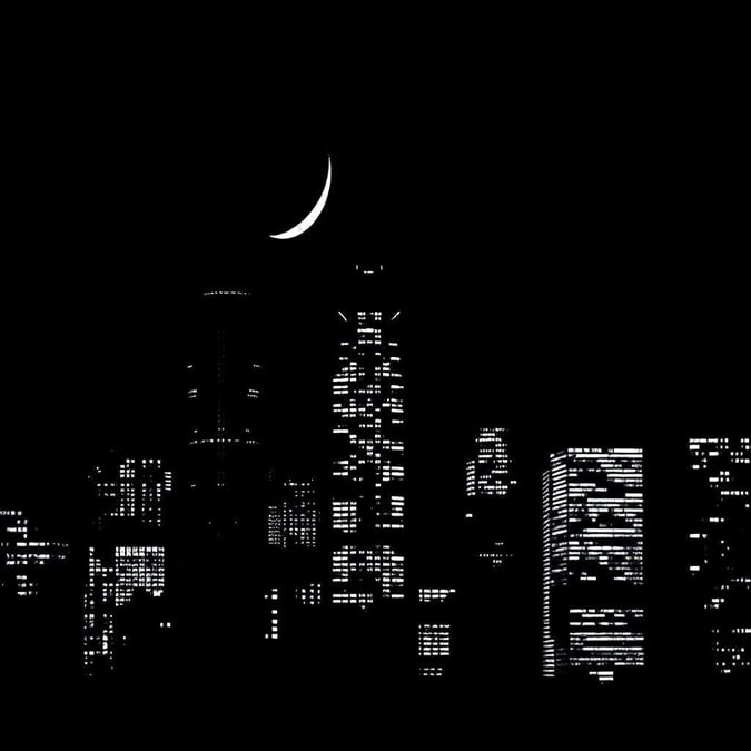 This image is a stunning black and white cityscape at night, featuring a crescent moon in the sky.