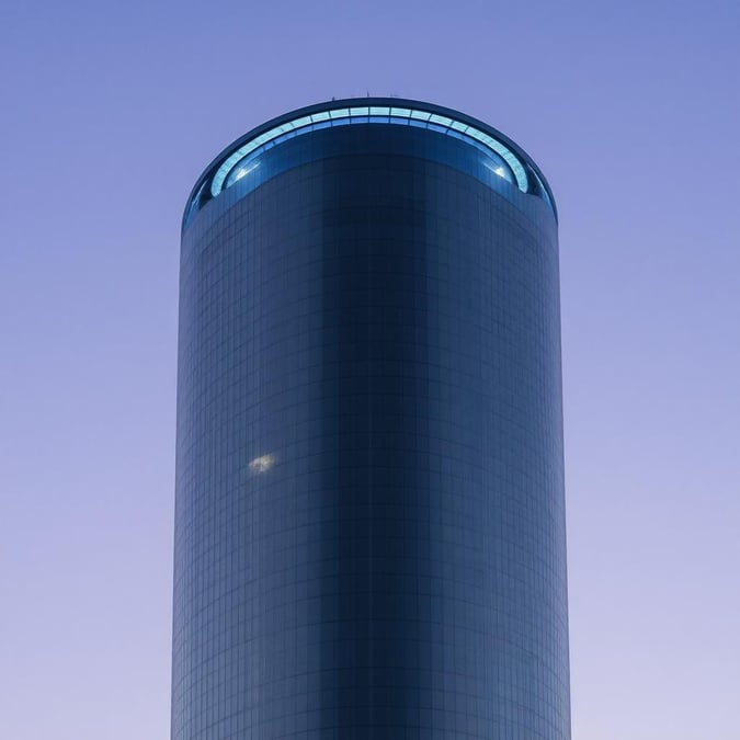 This anime-inspired skyscraper is a futuristic marvel, boasting a curved roof and a large circular window at the top. The building's dark gray hue is accentuated by a glimmering blue light, while two small lights on the roof add a touch of elegance. The bright white light in the bottom left corner and the bright lights on the right and left sides create a sense of depth and dimensionality.