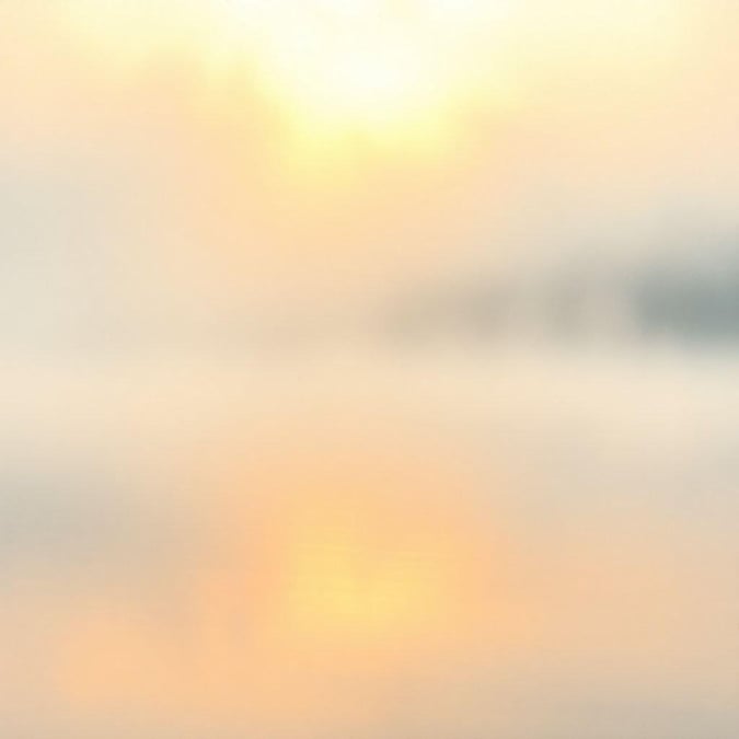 Sunrise or sunset creates a serene reflection on calm water, with a blurred background adding to the abstract beauty.